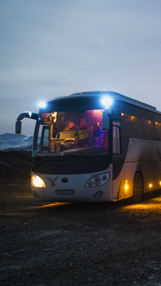 Coach bus with its lights on at dusk, mountains behind