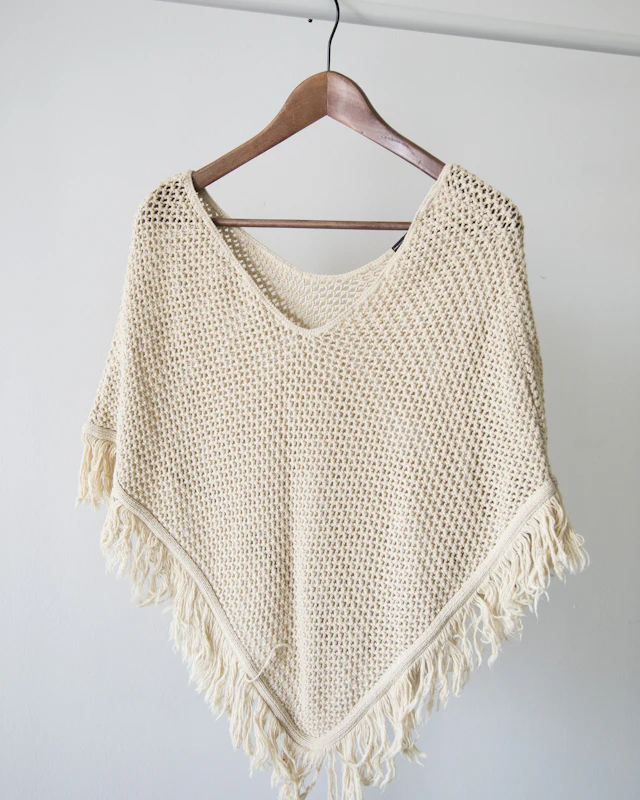 Ivory crochet knit poncho on a wooden hanger