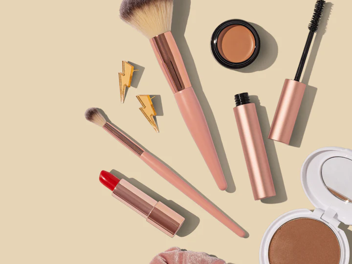 Makeup brushes, lipstick and compact powder on a beige background
